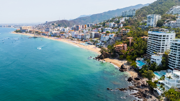Aerial view of sun kissed sands meet the turquoise embrace of the ocean where buildings cascade down hillsides Puerto Vallarta Jalisco Mexico.