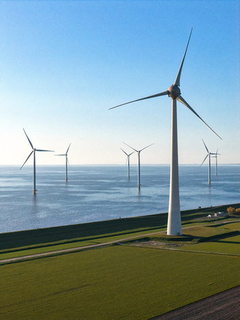 Aerial view of wind turbines standing in the sea and along a green coastline under a clear blue sky Netherlands.