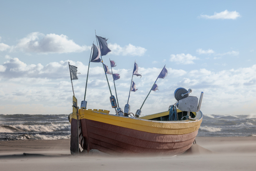 View of a traditional yellow and brown wooden fishing boat with flags on a sandy beach with waves in the background Debki Pomeranian Voivodeship Poland. View of a traditional yellow and brown wooden fishing boat with flags on a sandy beach with waves in the background Debki Pomeranian Voivodeship Poland.