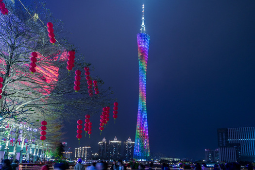 Guangzhou China 24 February 2024 View of Canton Tower illuminated with vibrant rainbow colors at night framed by red lanterns hanging from tree branches along the waterfront. Guangzhou China 24 February 2024 View of Canton Tower illuminated with vibrant rainbow colors at night framed by red lanterns hanging from tree branches along the waterfront.