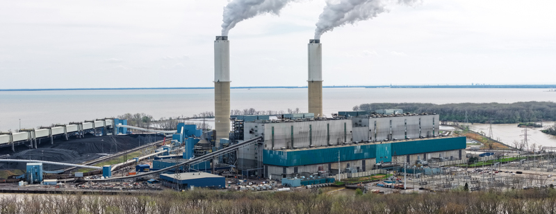 Aerial view of the Monroe Power Plant with two tall chimneys emitting smoke industrial structures coal piles and power lines along the waterfront in Monroe Michigan United States.