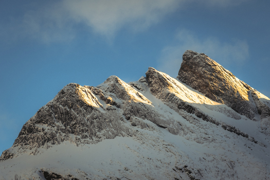 View of the majestic snow capped mountain peaks kissed by sunlight against a backdrop of serene blue sky Indregård Troms Norway. View of the majestic snow capped mountain peaks kissed by sunlight against a backdrop of serene blue sky Indregård Troms Norway.