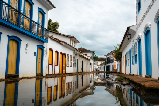 View of historic colonial buildings with colorful doors and windows reflected in a flooded cobblestone street under a cloudy sky in Paraty State of Rio de Janeiro Brazil. View of historic colonial buildings with colorful doors and windows reflected in a flooded cobblestone street under a cloudy sky in Paraty State of Rio de Janeiro Brazil.