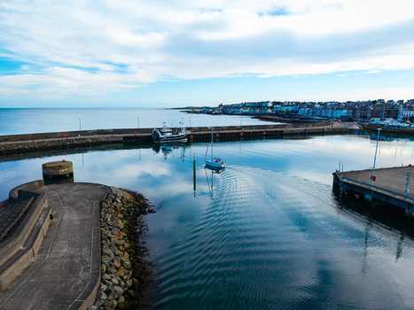 Aerial view of Bangor Harbour and Town with a sailboat navigating calm waters stone breakwaters and colorful buildings along the coastline in Bangor Northern Ireland United Kingdom.
