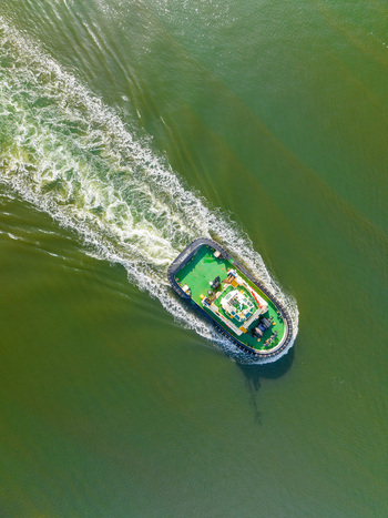 Aerial view of a tugboat moving through green water leaving a white wake in Williamstown Victoria Australia. Aerial view of a tugboat moving through green water leaving a white wake in Williamstown Victoria Australia.