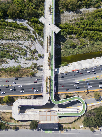 Aerial view of Paseo de la Mujer pedestrian bridge spanning over a busy highway with cars surrounded by lush green trees and urban infrastructure in Monterrey Nuevo Leon Mexico. Aerial view of Paseo de la Mujer pedestrian bridge spanning over a busy highway with cars surrounded by lush green trees and urban infrastructure in Monterrey Nuevo Leon Mexico.