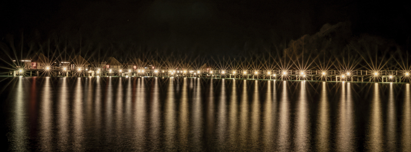 View of the illuminated overwater bungalows at Likuliku Lagoon Resort with bright lights reflecting on the calm ocean water at night in Yaro Nadroga Navosa Fiji.