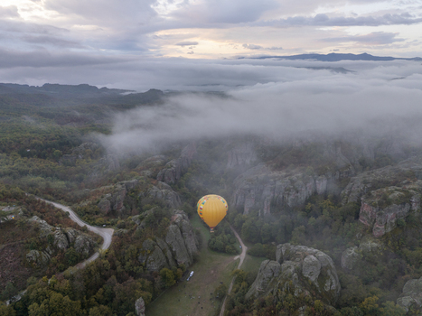 Aerial view of a yellow hot air balloon floating above the dramatic Belogradchik Rocks surrounded by low hanging clouds and autumn forest in Belogradchik Vidin Bulgaria.