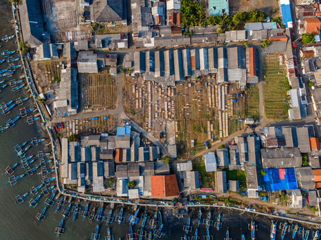 Aerial view of a coastal fishing village with small wooden boats moored along the shoreline rows of drying racks and dense residential housing in Cilacap Regency Central Java Indonesia. Aerial view of a coastal fishing village with small wooden boats moored along the shoreline rows of drying racks and dense residential housing in Cilacap Regency Central Java Indonesia.
