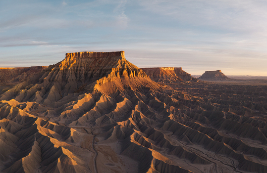 Aerial view of the rugged badlands and dramatic sandstone buttes of Caineville illuminated by the warm light of the golden hour in Caineville Utah United States.