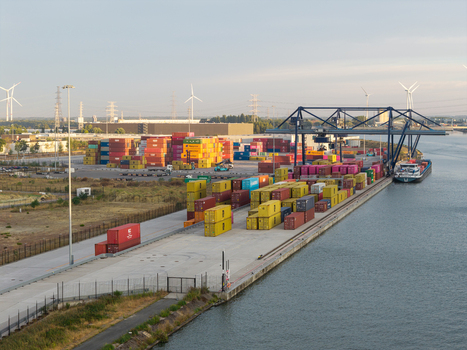 Genk Belgium 27 August 2026 Aerial view of Haven Genk container terminal with stacked shipping containers a cargo barge docked at the quay and wind turbines in the background. Genk Belgium 27 August 2026 Aerial view of Haven Genk container terminal with stacked shipping containers a cargo barge docked at the quay and wind turbines in the background.