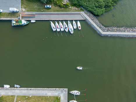 Aerial top view of sailboats moored in Port Tolkmicko marina with a small motorboat crossing the harbor on the Vistula Lagoon in northern Poland. Aerial top view of sailboats moored in Port Tolkmicko marina with a small motorboat crossing the harbor on the Vistula Lagoon in northern Poland.