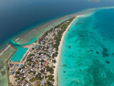 Aerial view of the island shows vivid turquoise waters meeting the sandy shore contrasting against the dark blue depths Vashafaru Island Thiladhummathi Atoll Maldives.
