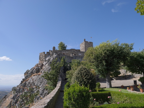 View of the historic stone walls and tower of Marvao Castle perched on a rocky cliff above a manicured garden under a clear blue sky in Marvao Portalegre District Portugal. View of the historic stone walls and tower of Marvao Castle perched on a rocky cliff above a manicured garden under a clear blue sky in Marvao Portalegre District Portugal.