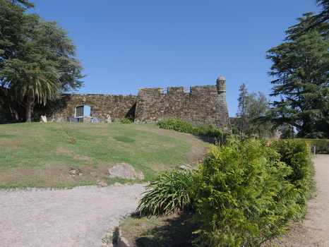 View of the historic stone walls and watchtower of Castelo do Castro surrounded by lush green lawns and trees under a clear blue sky in Vigo Pontevedra Spain.