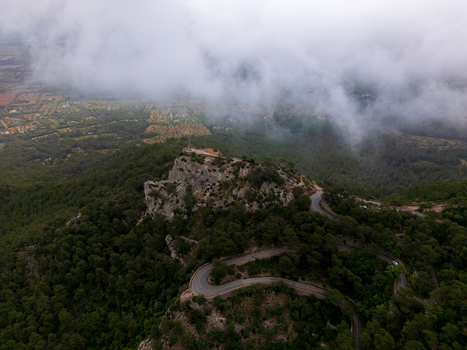 Aerial view of the Sanctuary of Sant Salvador on a mountain peak with a winding road and dense forest under thick clouds in Felanitx Illes Balears Spain. Aerial view of the Sanctuary of Sant Salvador on a mountain peak with a winding road and dense forest under thick clouds in Felanitx Illes Balears Spain.