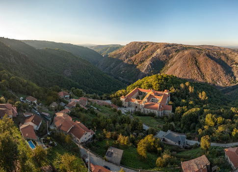 Aerial view of the Monastery of Santo Estevo de Ribas de Sil in the lush Ribeira Sacra hills with stone houses and terracotta rooftops in O Covelo Ourense Spain.