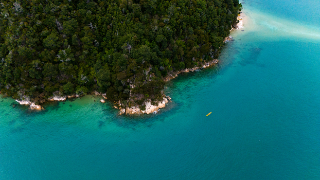 Aerial view of verdant forest meeting the turquoise sea a lone kayak adrift in the vast expanse Abel Tasman National Park Tasman Region New Zealand. Aerial view of verdant forest meeting the turquoise sea a lone kayak adrift in the vast expanse Abel Tasman National Park Tasman Region New Zealand.