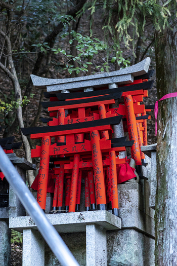 View of small red torii gates with black tops and Japanese inscriptions stacked on a stone pedestal in a wooded area at Senbon Torii Kyoto Kyoto Japan.