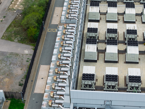 Aerial view of a data center roof featuring rows of industrial cooling units and HVAC equipment on a paved surface in the United Kingdom.