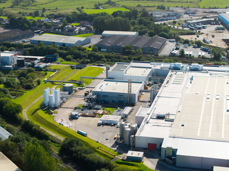 Aerial view of a large industrial manufacturing facility with white storage tanks metal rooftops and surrounding green fields in Lisburn Northern Ireland United Kingdom. Aerial view of a large industrial manufacturing facility with white storage tanks metal rooftops and surrounding green fields in Lisburn Northern Ireland United Kingdom.