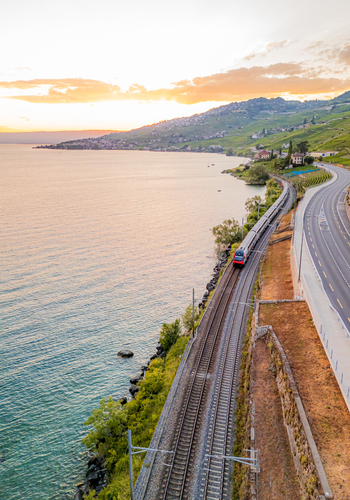 Aerial view of a train traveling along the railway tracks beside Lake Geneva with the terraced vineyards of the Lavaux region at sunset in Bourg en Lavaux Vaud Switzerland. Aerial view of a train traveling along the railway tracks beside Lake Geneva with the terraced vineyards of the Lavaux region at sunset in Bourg en Lavaux Vaud Switzerland.