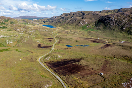 Aerial view of the rugged landscape of An Port featuring a winding road cutting through peat bogs rolling hills and small lakes under a blue sky Ardara County Donegal Ireland.