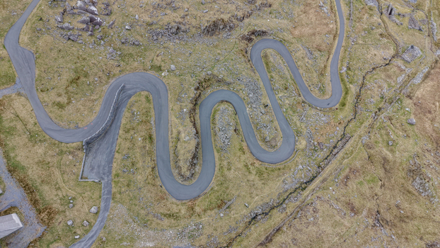 Aerial view of a winding road snaking through the rugged desolate landscape a ribbon of grey against the faded greens and browns of the terrain Blaenau Ffestiniog Wales United Kingdom. Aerial view of a winding road snaking through the rugged desolate landscape a ribbon of grey against the faded greens and browns of the terrain Blaenau Ffestiniog Wales United Kingdom.