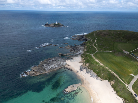 Aerial view of Godrevy Beach featuring the sandy shore rocky coastline and the Godrevy Lighthouse on an island in the distance at Gwithian England United Kingdom. Aerial view of Godrevy Beach featuring the sandy shore rocky coastline and the Godrevy Lighthouse on an island in the distance at Gwithian England United Kingdom.