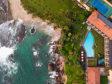 Aerial view of Gintota beach with turquoise waves crashing on rocks palm trees and a luxury resort with a swimming pool in Galle Southern Province Sri Lanka. Aerial view of Gintota beach with turquoise waves crashing on rocks palm trees and a luxury resort with a swimming pool in Galle Southern Province Sri Lanka.