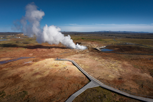 Aerial view of a geothermal area with a massive steam plume rising from a vent wooden walkways and people on a viewing platform Iceland.