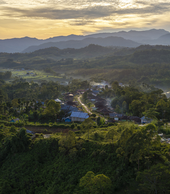 Aerial view of Bangka Kenda village nestled among lush green hills and misty mountains in the golden hour light in Wae Rii East Nusa Tenggara Indonesia.