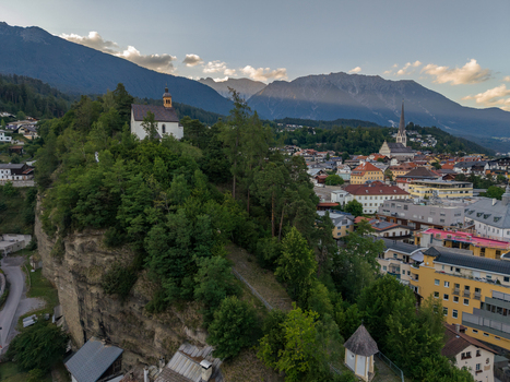 Aerial view of St. Laurentius Church perched on a rocky cliff overlooking the town of Imst with lush greenery and mountains in the background in Imst Tyrol Austria.