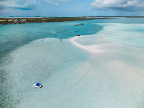 Aerial view of the Man O War Cay Sandbar with turquoise water boats anchored nearby and people walking on the white sand under a cloudy sky in Rolletown Exuma The Bahamas. Aerial view of the Man O War Cay Sandbar with turquoise water boats anchored nearby and people walking on the white sand under a cloudy sky in Rolletown Exuma The Bahamas.