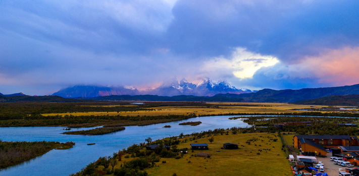 Aerial view of Rio Serrano Hotel and Spa and the winding Serrano River with snow capped mountains under a dramatic sky in Torres de Paine Magallanes y la Antar Chile. Aerial view of Rio Serrano Hotel and Spa and the winding Serrano River with snow capped mountains under a dramatic sky in Torres de Paine Magallanes y la Antar Chile.