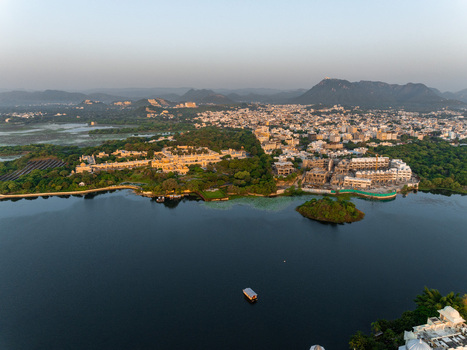 Aerial view of the historic City Palace and lush gardens along the shores of Lake Pichola in Udaipur Rajasthan India.