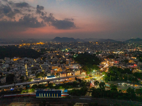Aerial view of the illuminated cityscape at dusk featuring dense urban architecture glowing street lights a railway station and distant hills in Udaipur Rajasthan India. Aerial view of the illuminated cityscape at dusk featuring dense urban architecture glowing street lights a railway station and distant hills in Udaipur Rajasthan India.