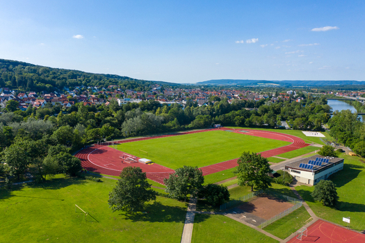 Aerial view of Sportinsel Forchheim featuring a red running track and green athletic field surrounded by lush trees and the town skyline in Forchheim Bayern Germany.