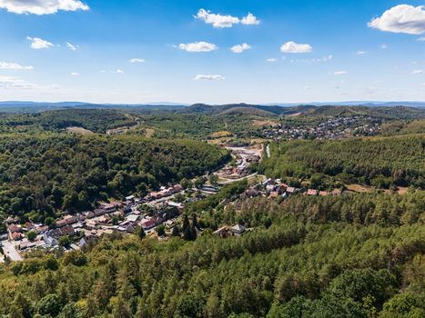 Aerial view of a residential district and quarry amid forested hills and valley terrain in Salgotarjan Hungary beneath a blue summer sky with scattered clouds. Aerial view of a residential district and quarry amid forested hills and valley terrain in Salgotarjan Hungary beneath a blue summer sky with scattered clouds.