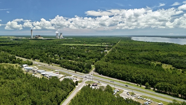 Aerial view of the Seminole Electric power plant with cooling towers near the St. Johns River surrounded by dense forests and a highway in Palatka Florida United States.