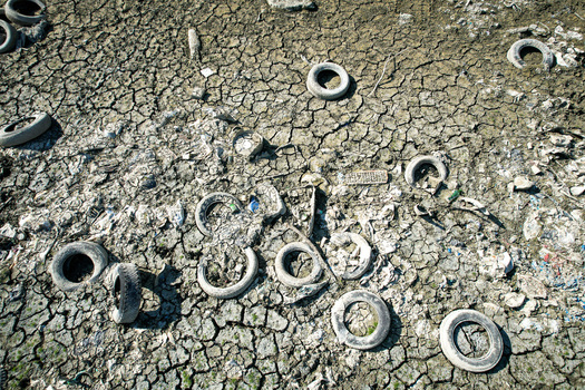 Aerial view of discarded tires and plastic trash scattered across a parched and cracked riverbed during a drought in Carignano Piemonte Italy. Aerial view of discarded tires and plastic trash scattered across a parched and cracked riverbed during a drought in Carignano Piemonte Italy.