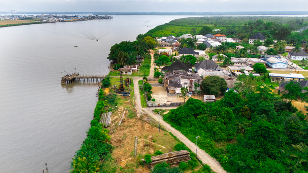 Aerial view of a riverfront settlement with houses a wooden pier and lush vegetation along the riverbank in Rivers Nigeria.