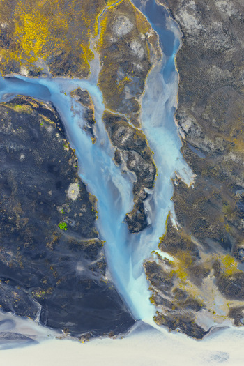 Aerial view of a glacial river winding through dark volcanic terrain with patches of mossy green vegetation in Selfoss Sveitarfelagid Arborg Iceland. Aerial view of a glacial river winding through dark volcanic terrain with patches of mossy green vegetation in Selfoss Sveitarfelagid Arborg Iceland.