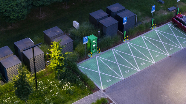 Aerial view of an electric vehicle charging station with green parking spaces marked with EV symbols surrounded by landscaping and utility units in Poland. Aerial view of an electric vehicle charging station with green parking spaces marked with EV symbols surrounded by landscaping and utility units in Poland.
