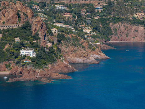 Aerial view of Le Trayas featuring dramatic red rocky cliffs lush Mediterranean vegetation and scattered villas overlooking the deep blue sea Saint Raphael Provence Alpes Cote d Azur France. Aerial view of Le Trayas featuring dramatic red rocky cliffs lush Mediterranean vegetation and scattered villas overlooking the deep blue sea Saint Raphael Provence Alpes Cote d Azur France.