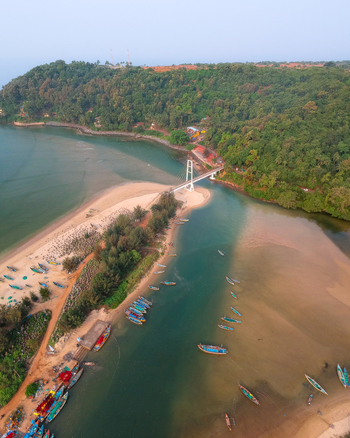 Aerial view of the suspension bridge over the Vengurla estuary featuring numerous colorful fishing boats moored along the sandy banks and lush green hills in Vengurla Maharashtra India. Aerial view of the suspension bridge over the Vengurla estuary featuring numerous colorful fishing boats moored along the sandy banks and lush green hills in Vengurla Maharashtra India.