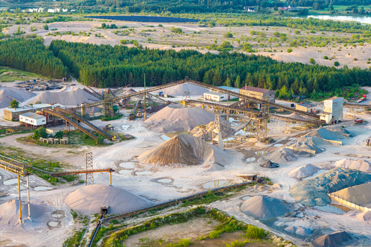 Aerial view of a large scale sand and gravel mine featuring industrial conveyor belts piles of processed aggregate and processing facilities surrounded by forest in Poland.