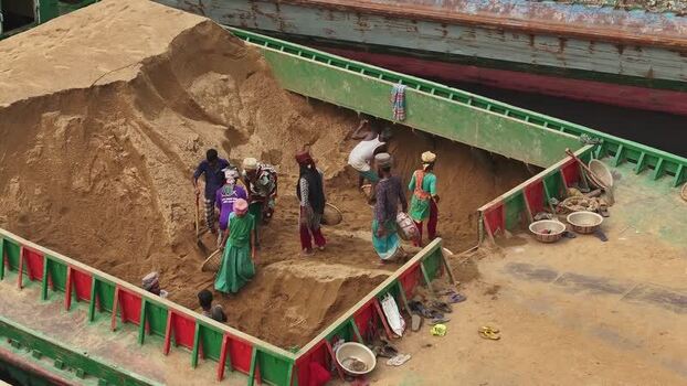 Aerial view of workers shoveling sand on a barge in Dhaka Bangladesh. Aerial view of workers shoveling sand on a barge in Dhaka Bangladesh.