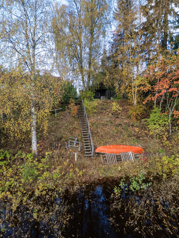 Aerial view of an autumn landscape along a riverbank with vibrant fall foliage a wooden staircase and an orange boat resting on the shore Muhos North Ostrobothnia Finland. Aerial view of an autumn landscape along a riverbank with vibrant fall foliage a wooden staircase and an orange boat resting on the shore Muhos North Ostrobothnia Finland.