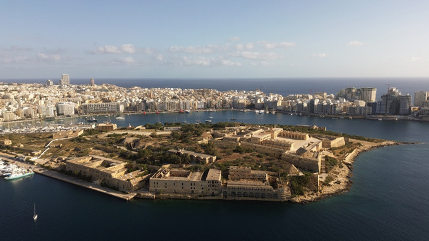 Aerial view of the historic fortifications of Fort Manoel on an island in the harbor with the Valletta skyline in the background surrounded by blue waters in Valletta Port Region Malta. Aerial view of the historic fortifications of Fort Manoel on an island in the harbor with the Valletta skyline in the background surrounded by blue waters in Valletta Port Region Malta.